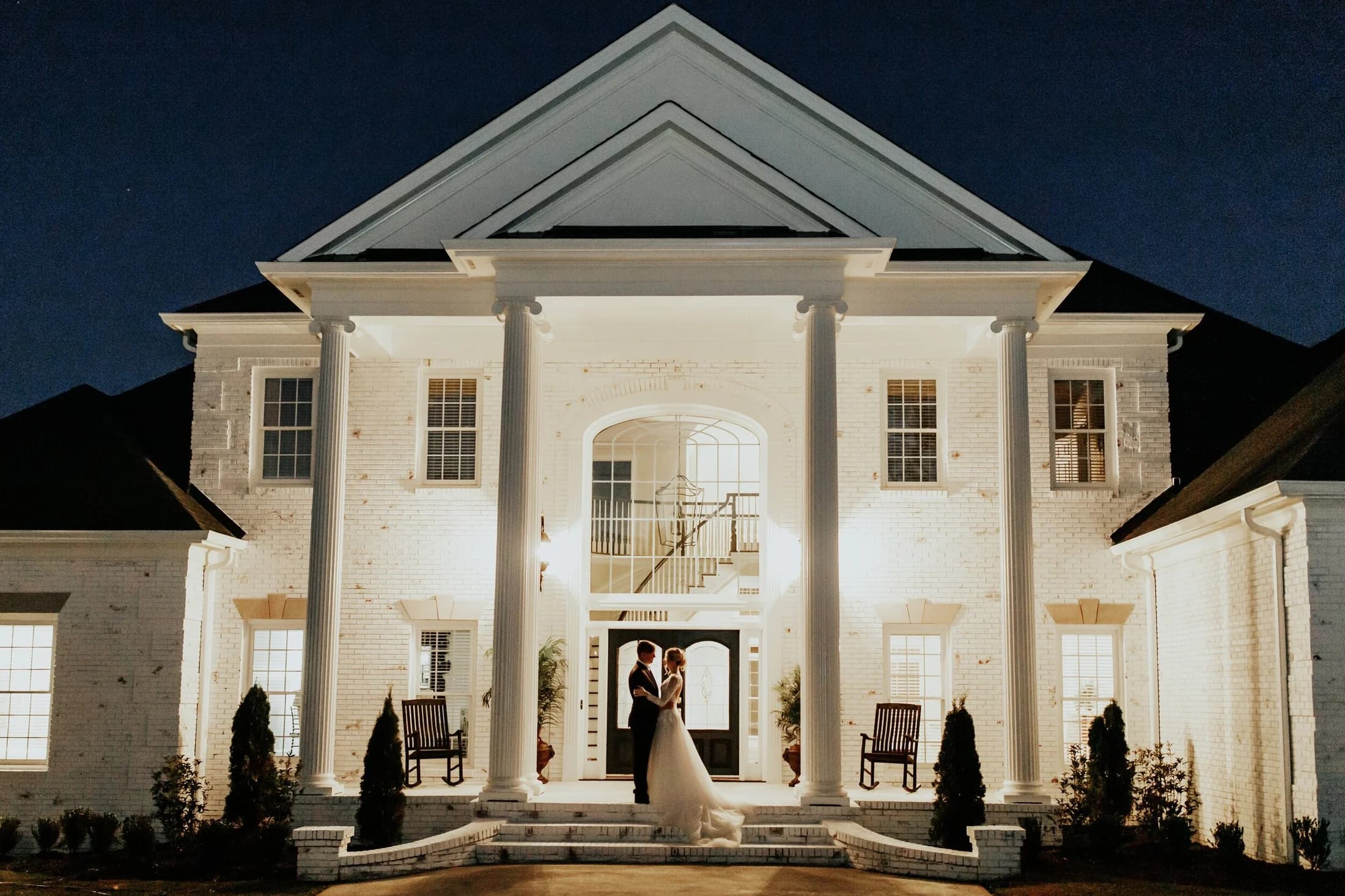 A couple beneath the lit columns of the mansion at night