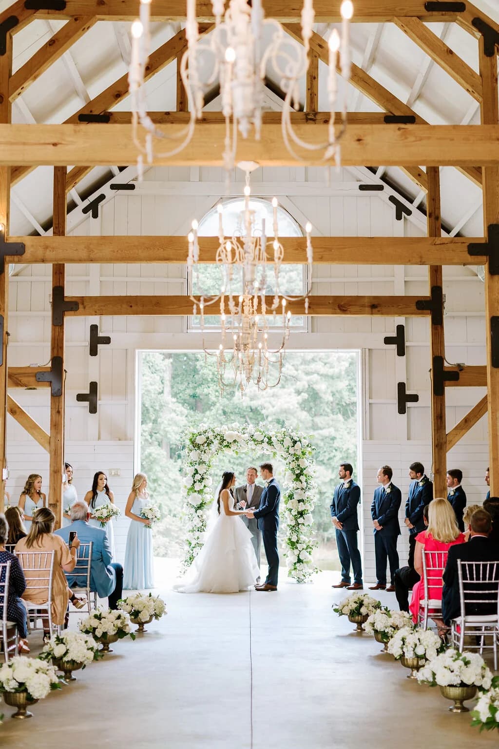 A wedding ceremony in the white barn with guests seated on both sides